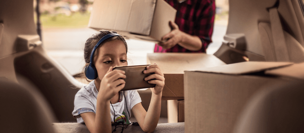 Child playing with electronic device near boxes on moving day.